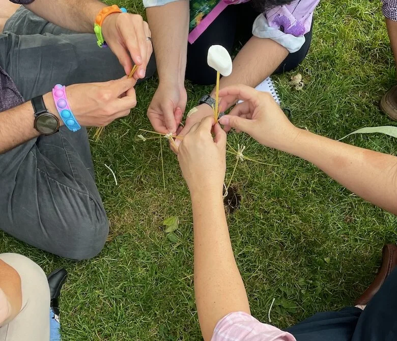 Hands assembling a spaghetti and marshmallow structure during a workshop exercise